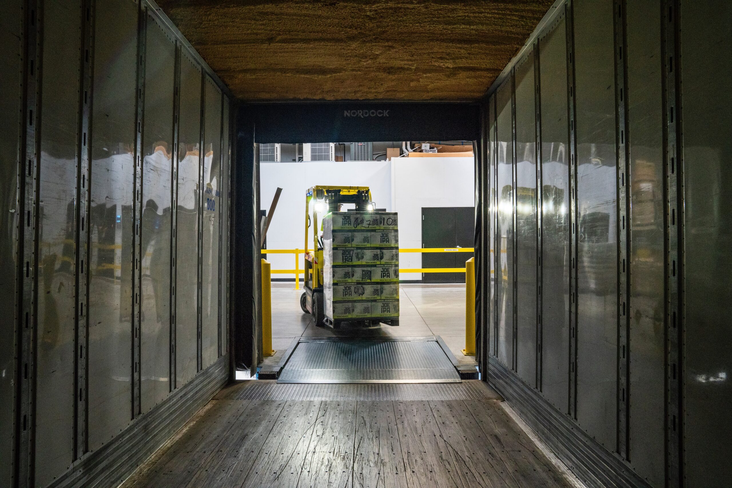 Forklift moving in an aisle of the warehouse with a bundle of the products.